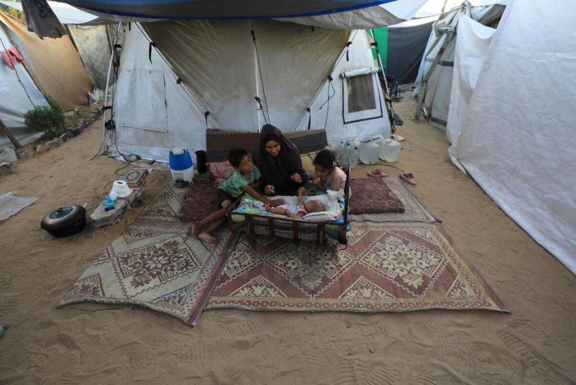 أم مع أطفالها الثلاثة في مخيم للنازحين غرب غزة
